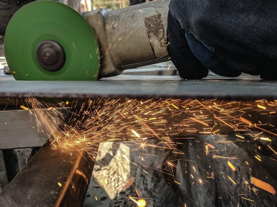 A gloved hand running a green cut-off wheel through steel, throwing a fan of sparks