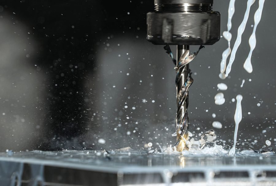 A twist drill boring into aluminum plate under a stream of milky coolant