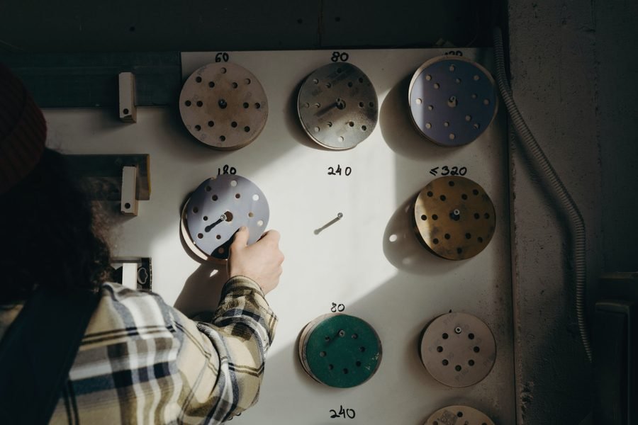 A worker in a flannel shirt choosing a sanding disc from a wall board marked by grit