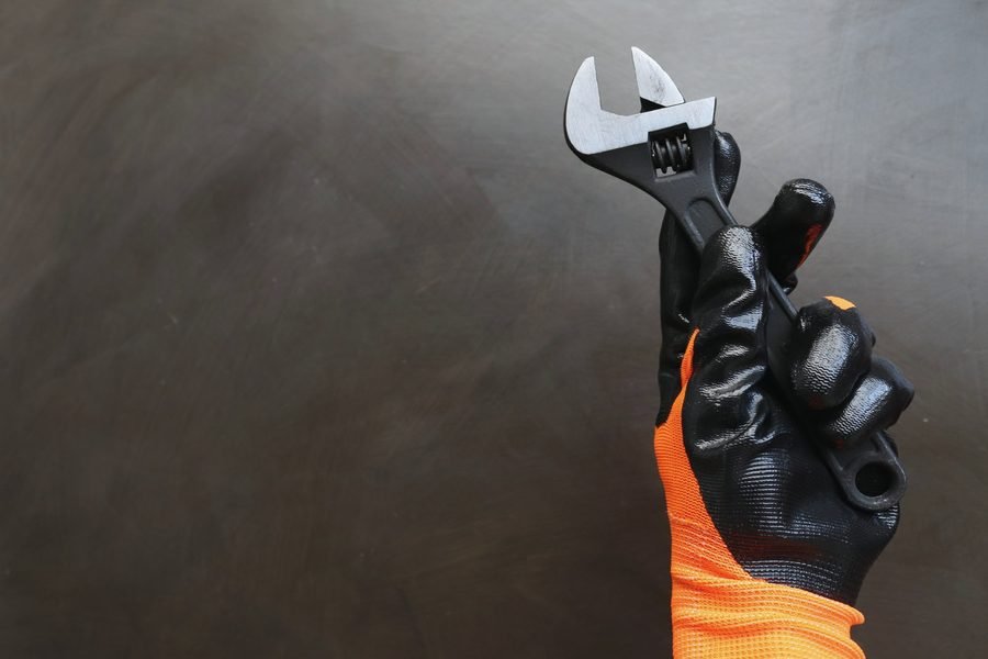 A hand in an orange and black coated work glove holding an adjustable wrench